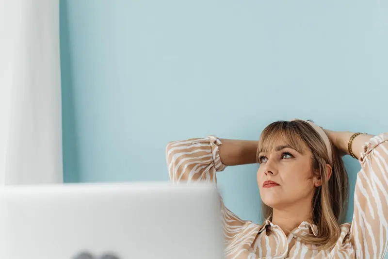 Une femme détendue se penche en arrière à son bureau, les mains derrière la tête
